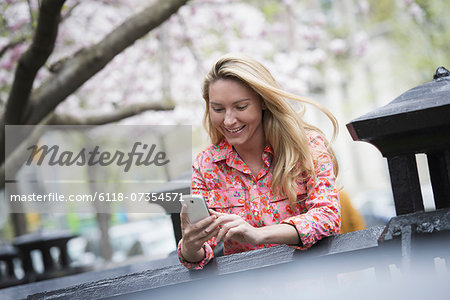 City life in spring. A young woman with long blonde hair sitting in a city park, looking at her smart phone.