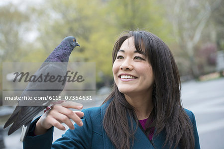 A young woman in the park with a pigeon perched on her wrist.