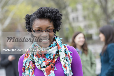 A group of people in a city park. A young woman smiling, wearing a purple shirt and floral scarf.