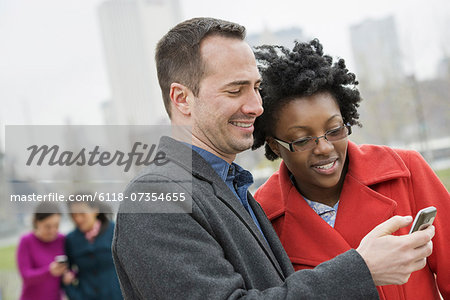 A cityscape, view to Manhattan from Brooklyn. Four people, two in the background and two checking a phone.