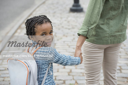 A New York city park in the spring. Sunshine and cherry blossom. A boy wearing a school bookbag, and walking hand in hand with a woman.