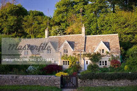 Terrace of traditional Cotswolds stone cottages with front gardens in  Bibury, The Cotswolds, Gloucestershire, UK