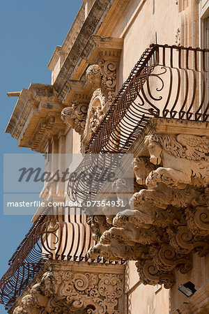 Baroque stone carvings of heads under a balcony at the Palazzo Nicolaci di Villadorata in Noto, UNESCO World Heritage Site, Syracuse Province, Sicily, Italy, Europe