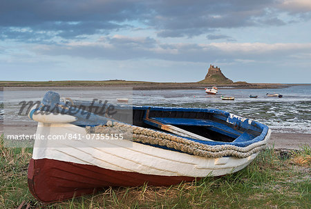 Fishing boat pulled onto the shore at Holy Island, looking towards the castle, Lindisfarne, Northumberland, England, United Kingdom, Europe Fishing boat pulled onto the shore at Holy Island, looking towards the castle, Lindisfarne, Northumberland, England, United Kingdom, Europe