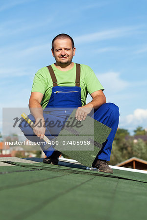 Worker installing bitumen roof shingles in summer time