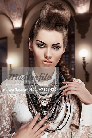 fashion portrait of sexy young brunette woman with amazing creative style, original hair-style and pretty make-up. Wearing white lace shirt and a lot of necklaces