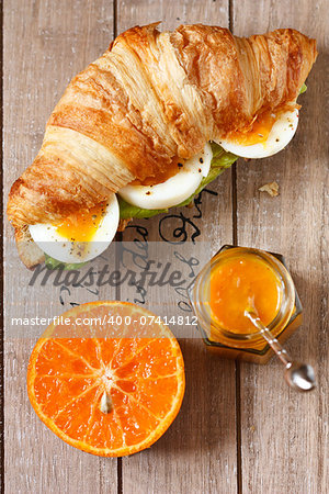 Croissant sandwich with egg, orange fruit and marmalade for breakfast on a wooden board.