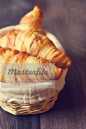 Fresh croissants for breakfast in a basket on a wooden background. Toned photo.