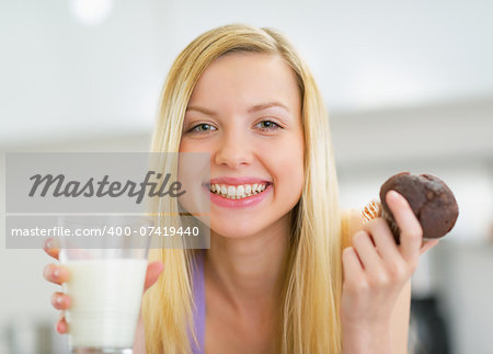 Portrait of happy young woman with milk and chocolate muffin in kitchen