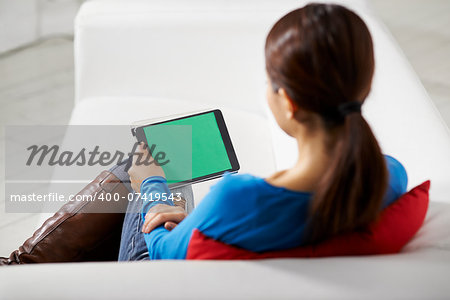 portrait of beautiful asian girl using tablet pc with green screen, sitting on sofa at home
