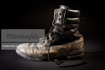 old soldier's boots worn with scratches and untied shoelaces on black background