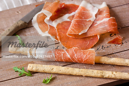 Grissini bread sticks with prosciutto ham and arugula on wooden board.