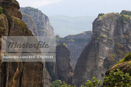 Assemblage of rocks intersperses with green trees. These are Meteora rock pillars in Greece.