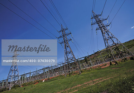 pillars with electricity transmitting lines in field under blue skies