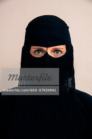 Close-up portrait of woman wearing black muslim hijab and muslim dress, looking at camera, studio shot on white background