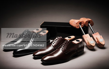 Black and Brown Pairs of Shoes with Shoe Trees and Box on Gray Background
