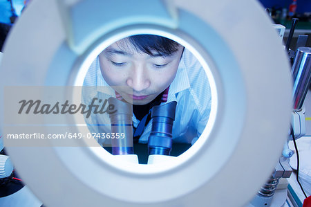 Worker at small parts manufacturing factory in China looking through microscope