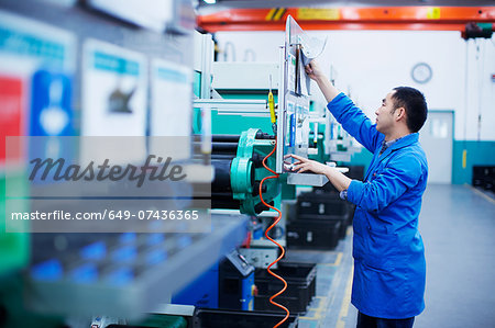 Worker at small parts manufacturing factory in China, reaching up to press button on control panel