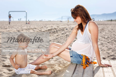 Baby on beach tipping sand onto mother's hand