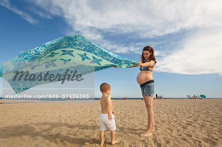 Pregnant woman on beach with blanket waving in wind