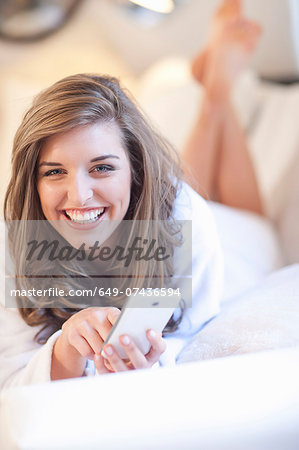 Portrait of young woman lying on bed with mobile phone