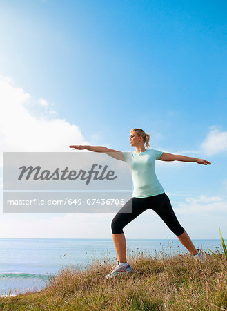 Mid adult woman stretching on cliff top, Thurlestone, Devon, UK