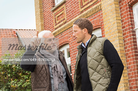 Father and son outside building, senior man pointing