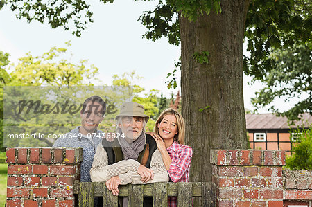 Portrait of senior man with mid adult couple leaning on gate