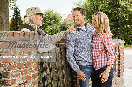 Senior man leaning on gate talking to with mid adult couple