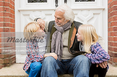 Grandfather sitting with grandchildren on front doorstep