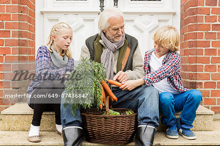 Grandfather sitting with grandchildren on doorstep with carrots