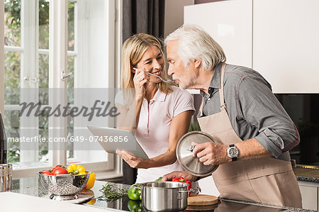 Senior man cooking with daughter, tasting food