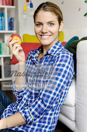 Portrait of young woman sitting on floor holding an apple