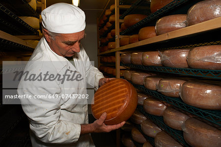 Senior man checking cheese round at farm factory