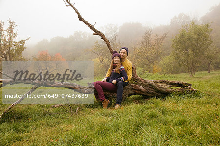Young couple sitting on bare tree in misty park