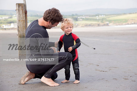 Father and son on beach wearing wet suits