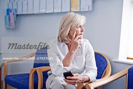 Mature female patient with mobile phone in hospital waiting room