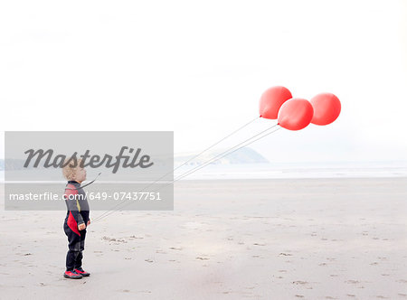 Portrait of boy on beach with red balloons