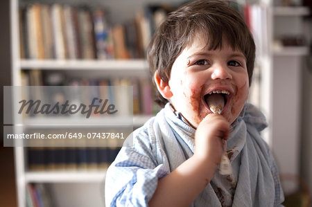 Portrait of male toddler licking chocolate covered teaspoon