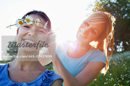 Mother tying daisy chain around daughter's head