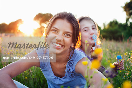 Portrait of girls sitting in field, one blowing bubbles