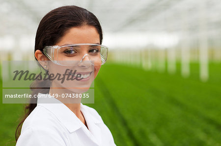 Scientist wearing goggles in front of plants in greenhouse