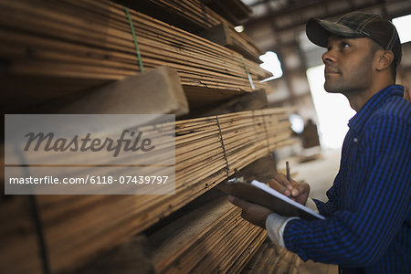 A heap of recycled reclaimed timber planks of wood. Environmentally responsible reclamation in a timber yard. A man with a clipboard by a rack of planks.