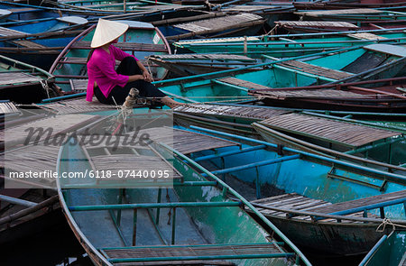 Lost in thought, a woman sits amidst a raft of boats. Ninh Binh, Vietnam