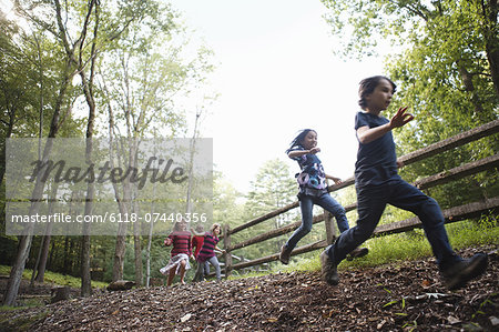 Three children playing around the farm, running around a paddock with wooden fencing.