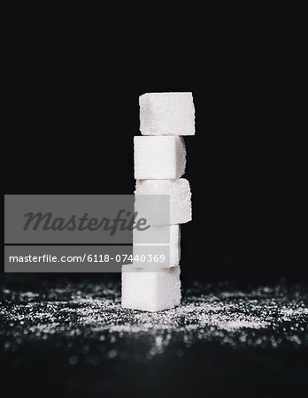 Stack of sugar cubes, balancing one on top the other, on black backdrop