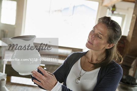 A woman holding a white pottery jug in an antique goods and furniture store.