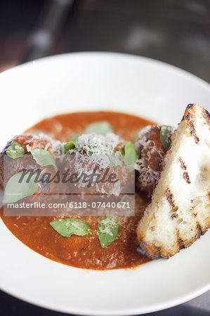 A dish of organic freshly prepared food. Grass-fed beef meatballs in tomato sauce with herb basil, shavings of Parmesan cheese and grilled bread.