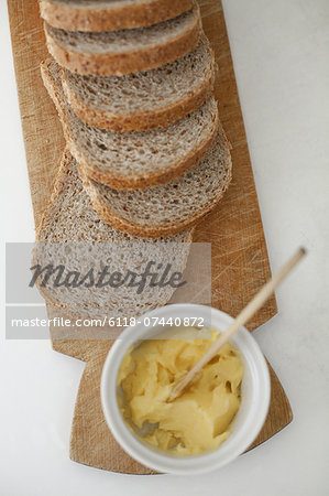 A wooden breadboard with a sliced brown loaf laid out. A dish of butter with a wooden butter knife.