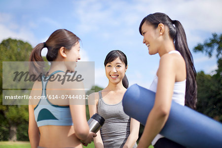 Three young women preparing for yoga practice in park